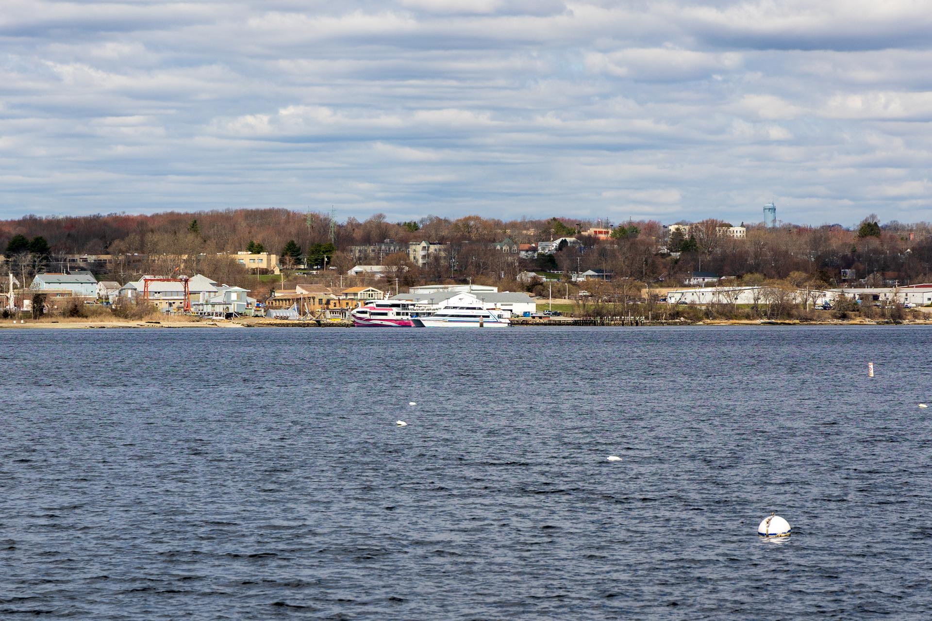 Wide water view with boats docked at distant shore under cloudy sky.