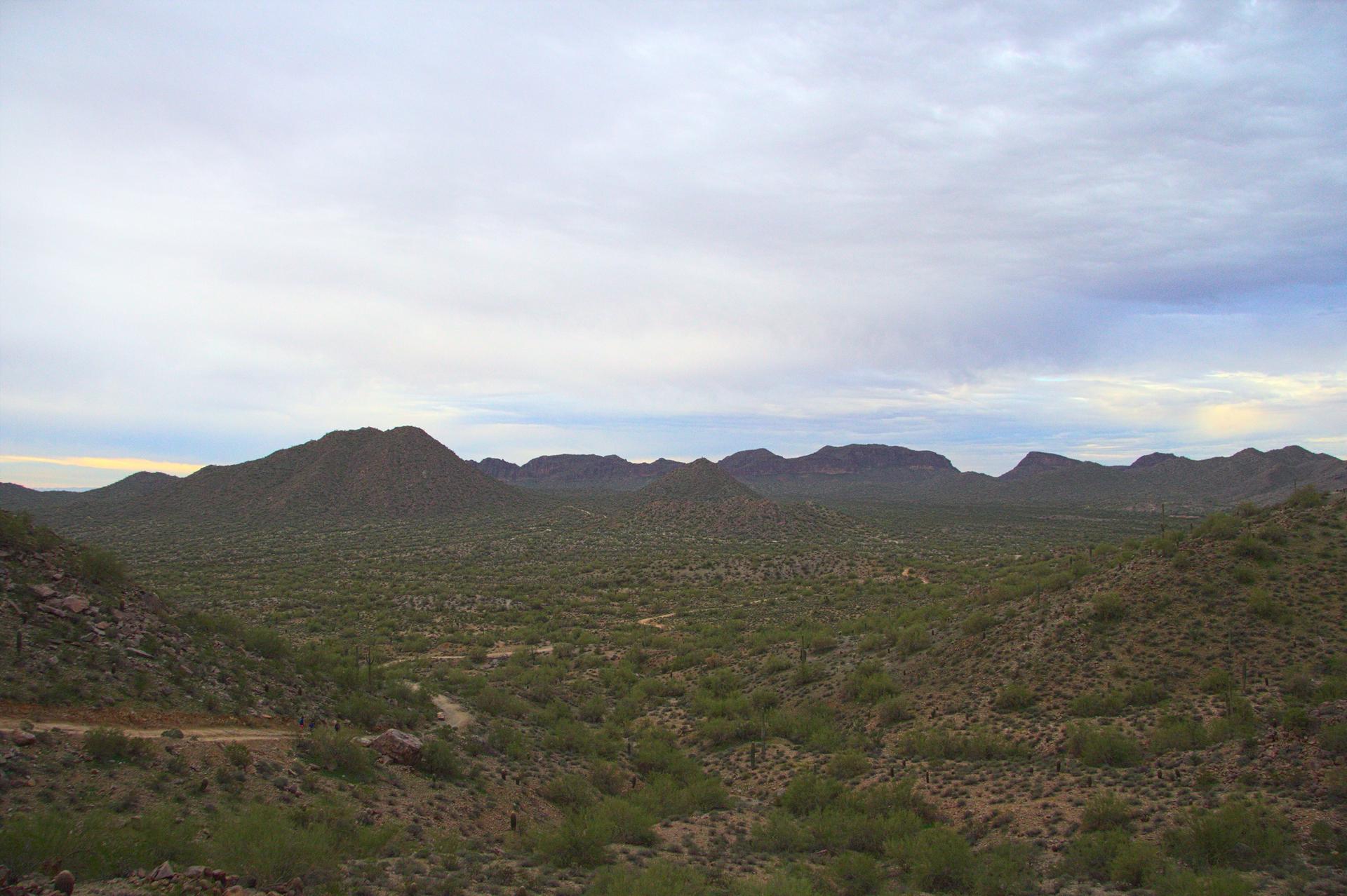 Vast desert landscape with rolling hills and distant mountains under a cloudy sky.
