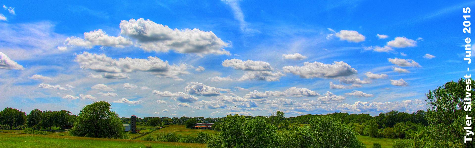 Expansive green landscape under a bright blue sky with scattered white clouds.