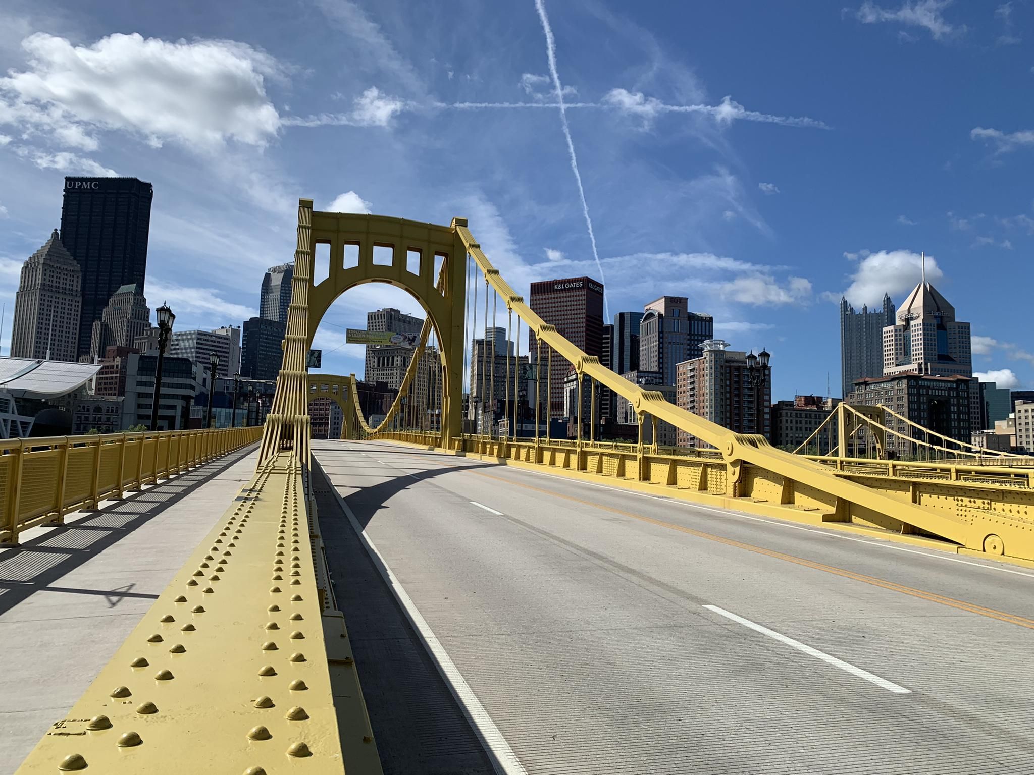 Empty yellow bridge leading to a city skyline under a bright blue sky. - North Shore Trail