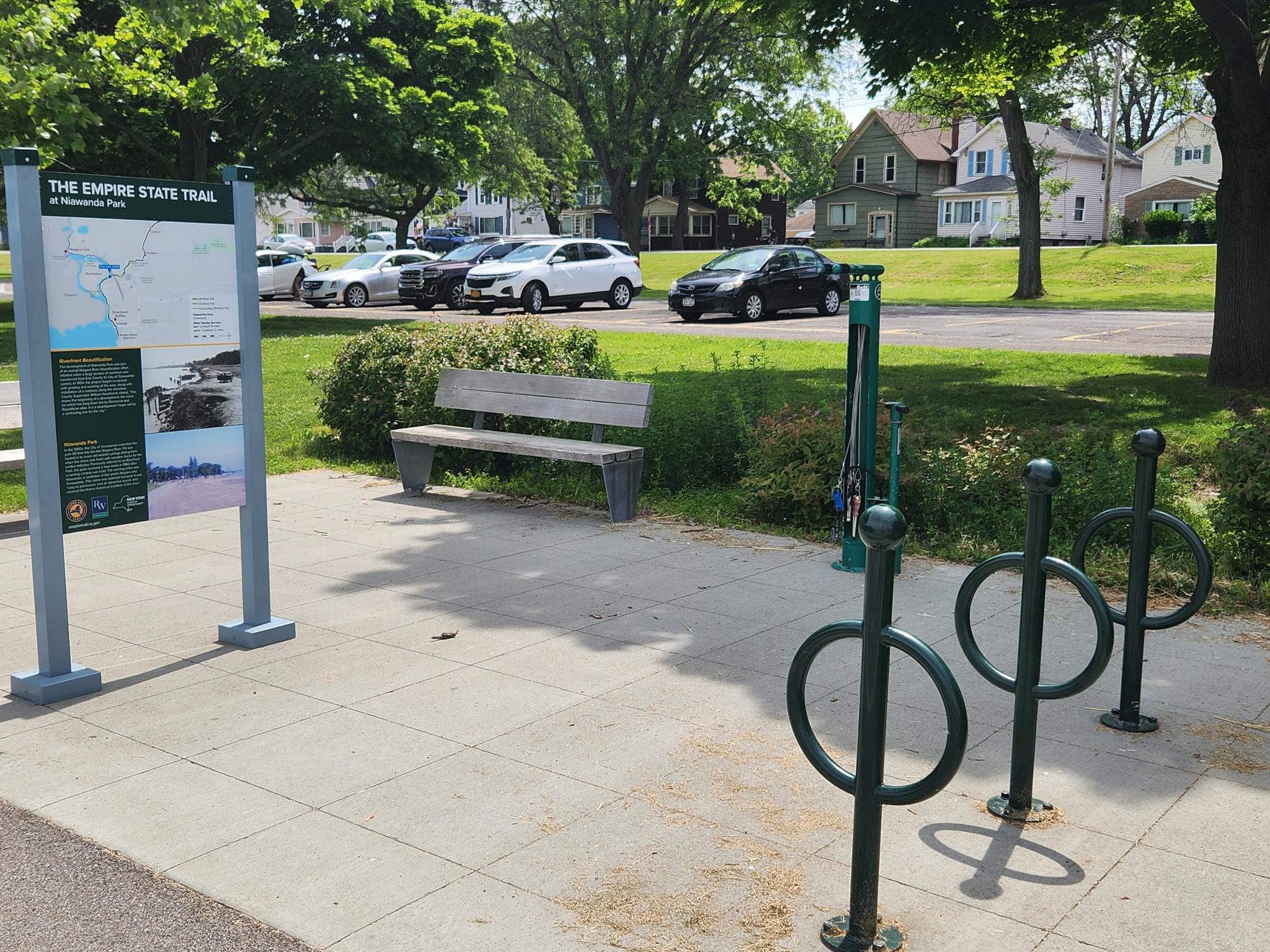 An information sign, wooden bench, and bike racks in a park setting.