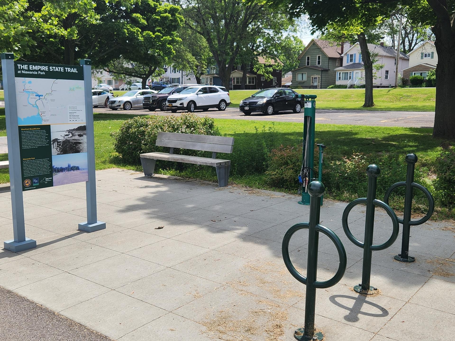 An information sign, wooden bench, and bike racks in a park setting.