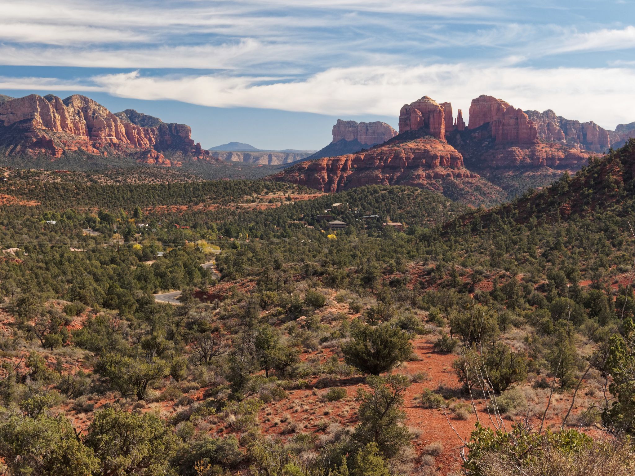 Vast desert landscape with green shrubs, red rock formations, and a cloudy sky. - Red Rock Loop