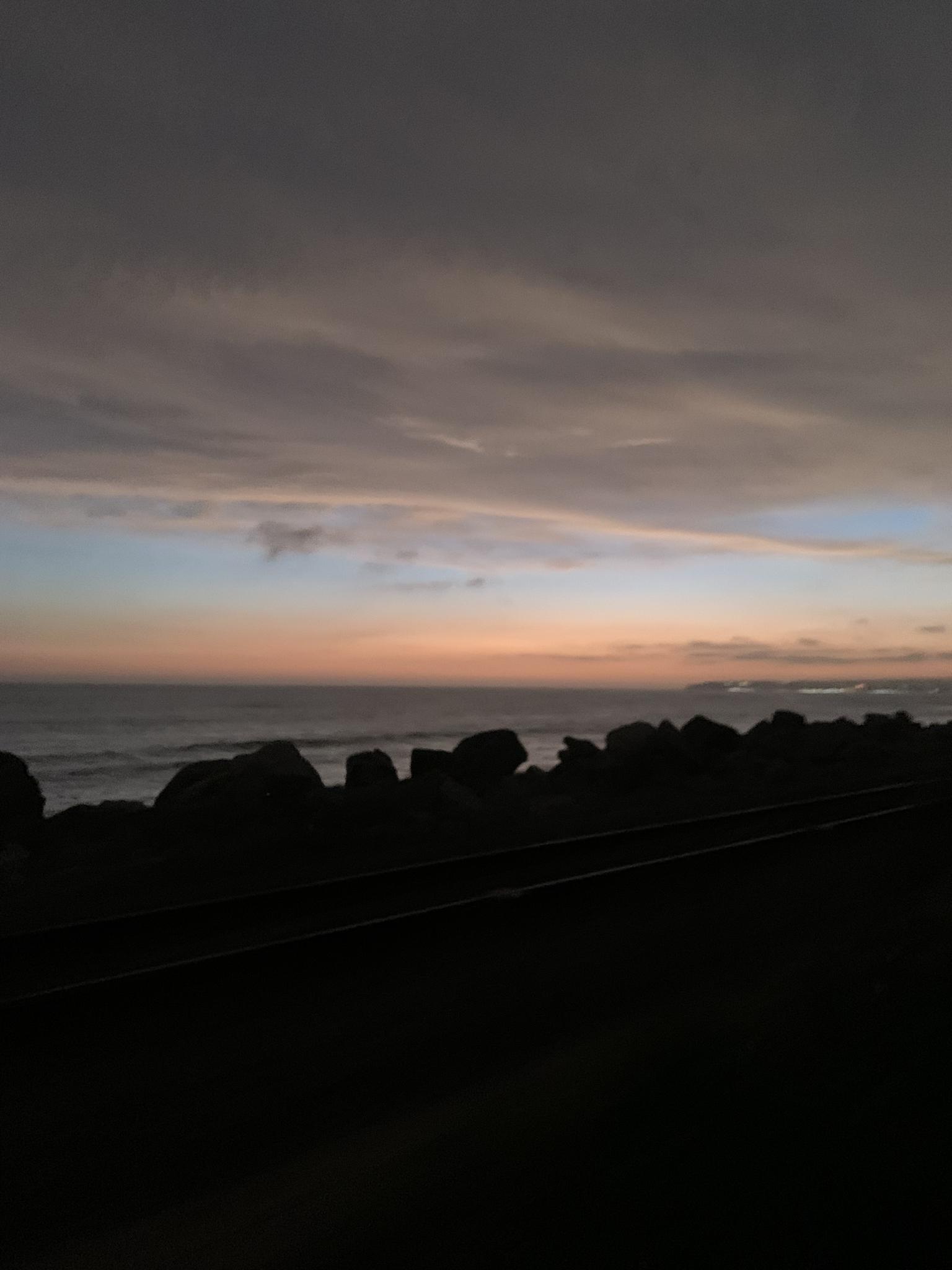 Dark silhouette of rocks and tracks at sunset over the ocean.