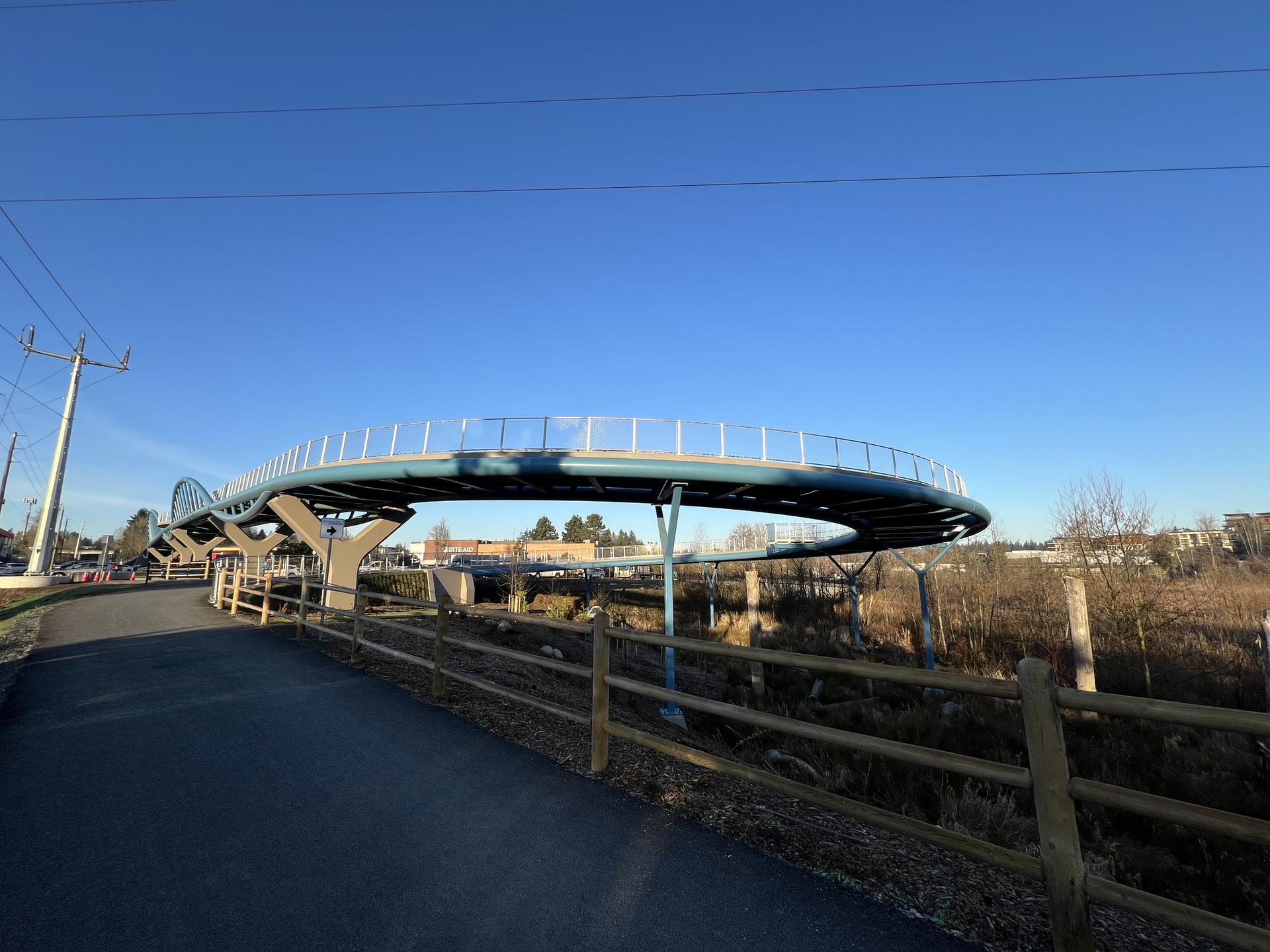 Modern curved pedestrian bridge over a path under a clear blue sky.