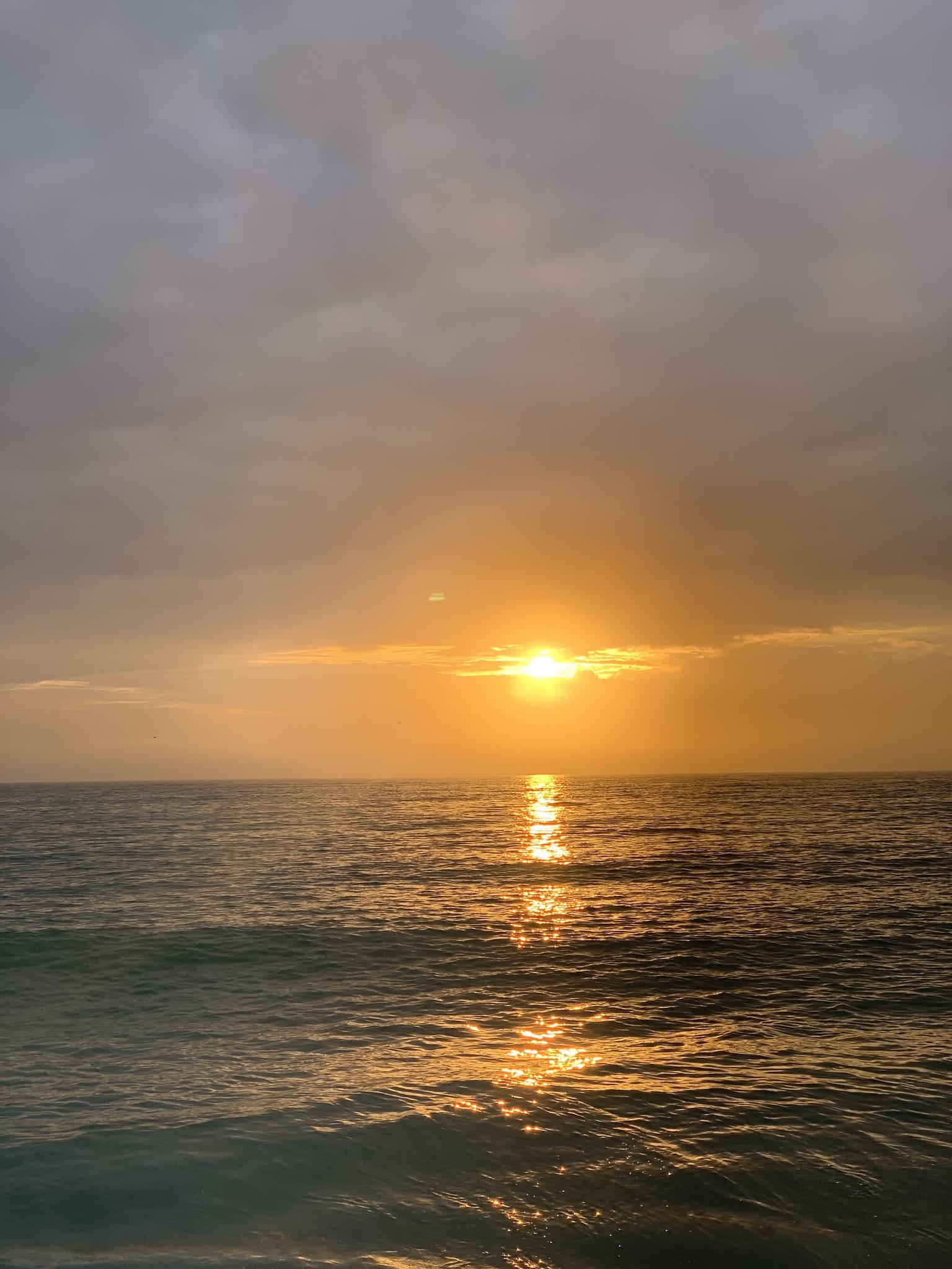 Golden sunset over a calm ocean with a cloudy sky.