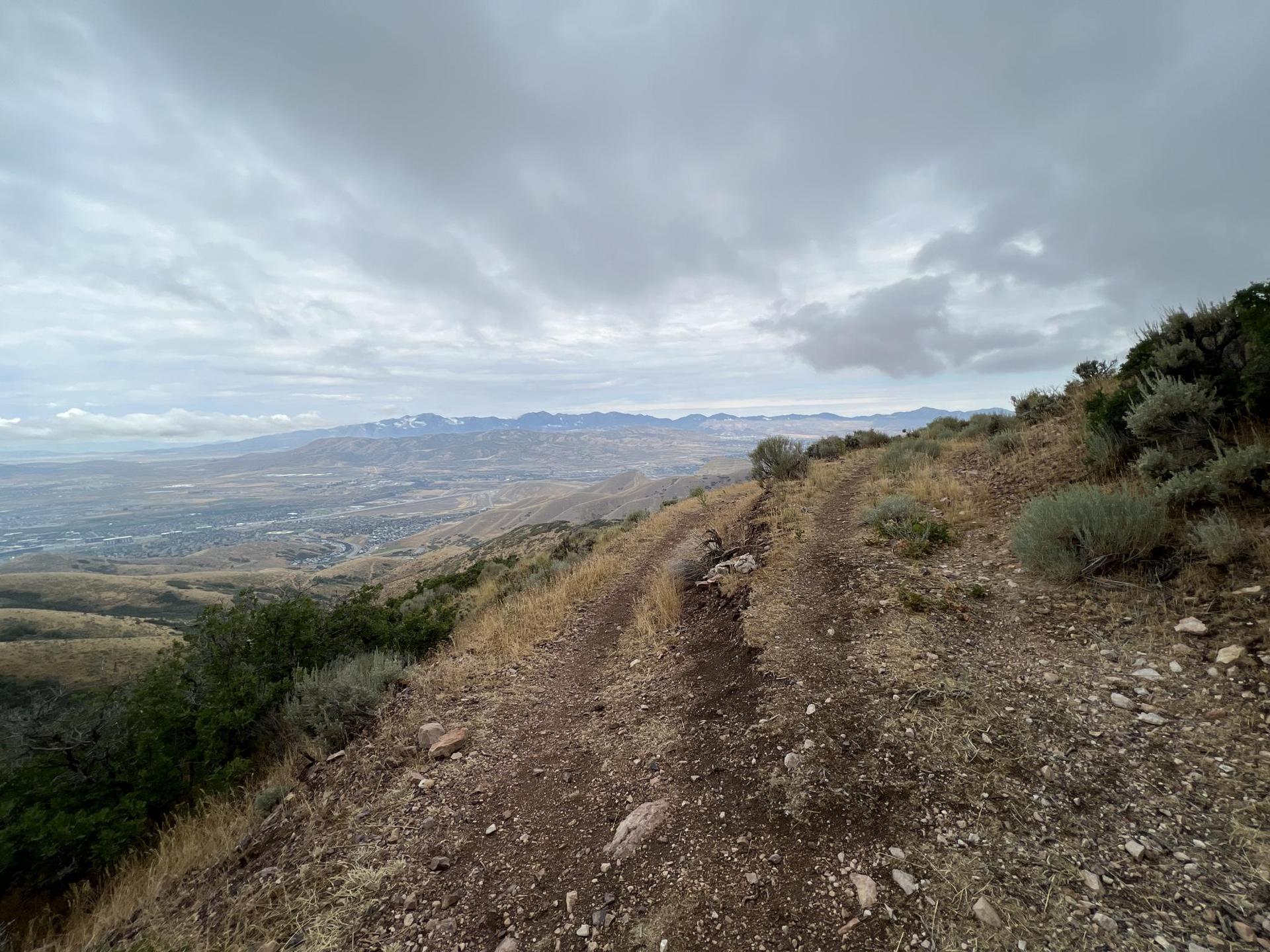 Dirt trail winding along a dry, rocky hillside under an overcast sky.