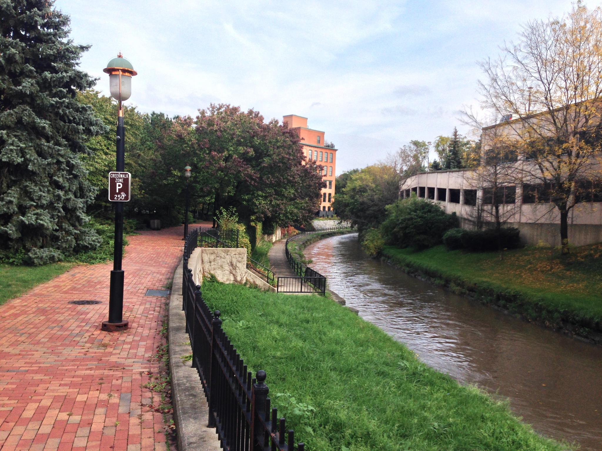 Brick path next to a canal, with trees and buildings under an overcast sky.