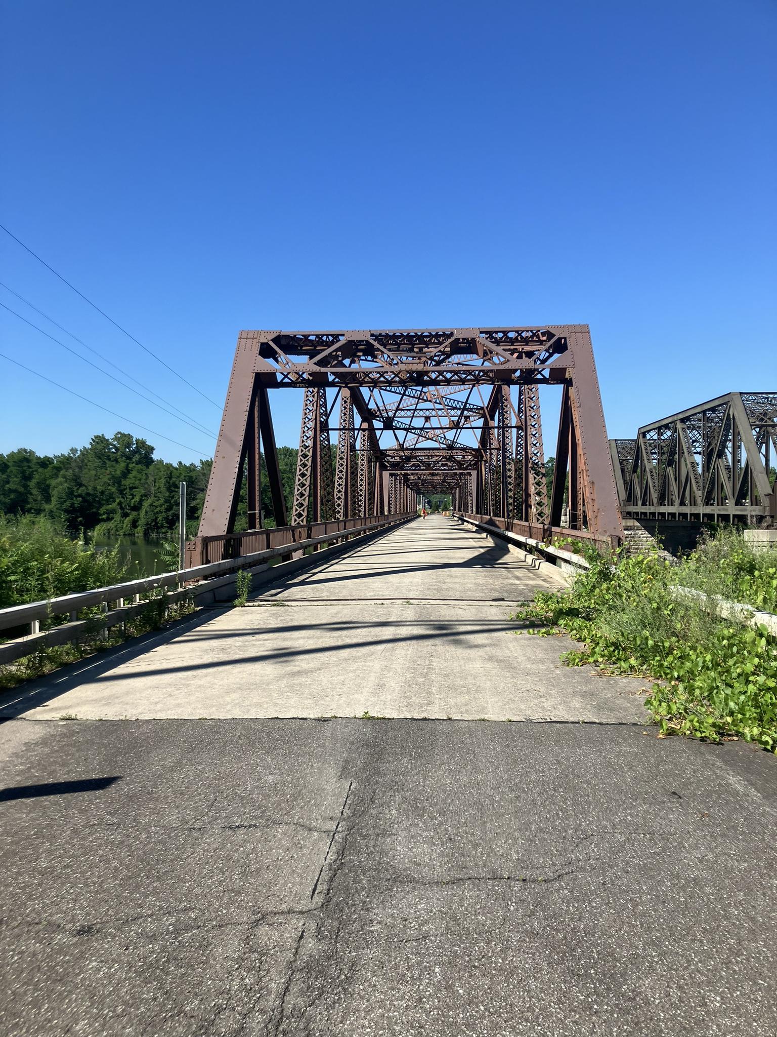Long, rusty metal truss bridge stretching into the distance under a clear sky.