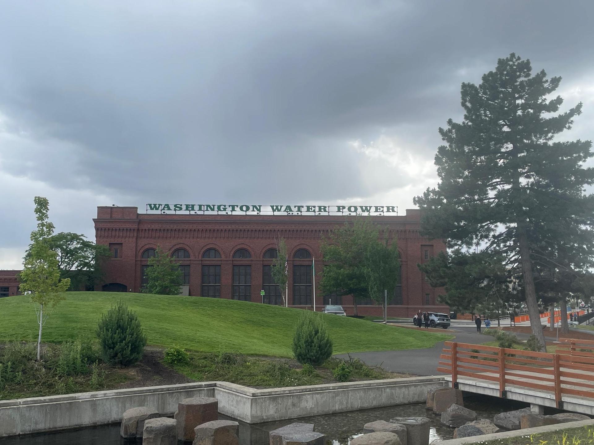 Large brick building with a sign, green lawn, and a cloudy sky.