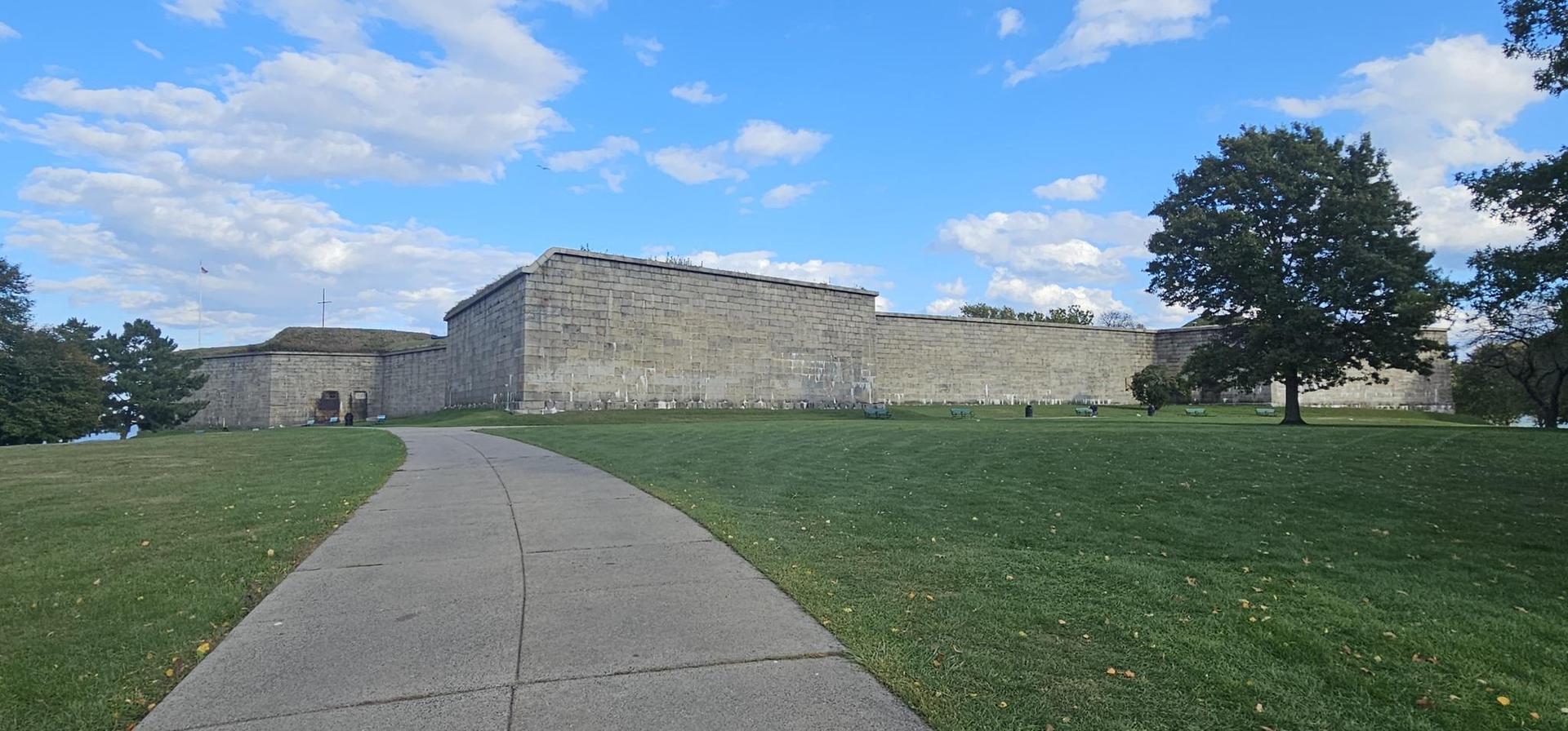 Large stone building with a paved path and green lawn under a cloudy sky.