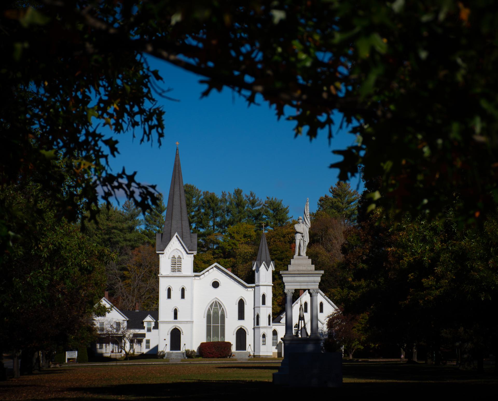 White church with a tall steeple framed by trees on a sunny day.