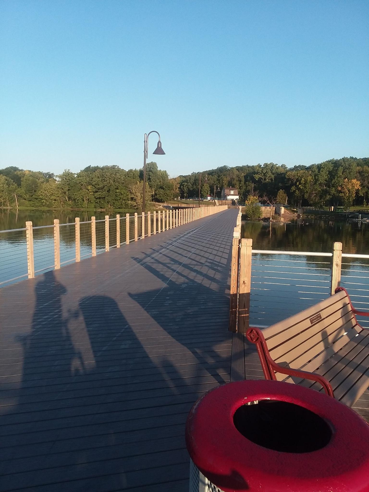 Long wooden pier over water under a clear, sunny sky with shadows.