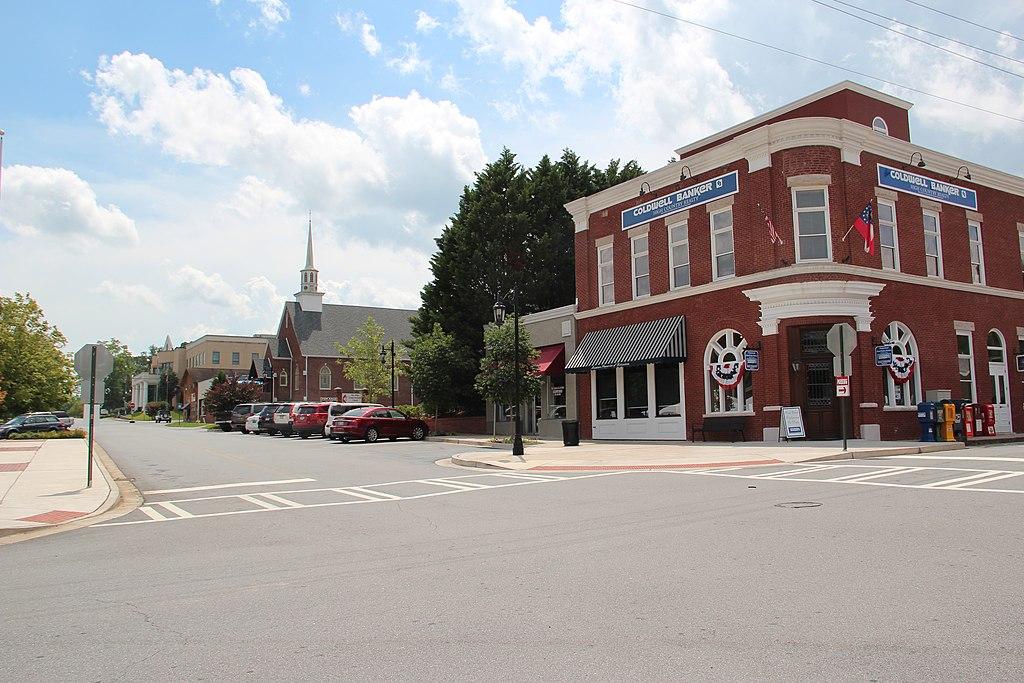 A brick corner building and street with a church under a cloudy sky.