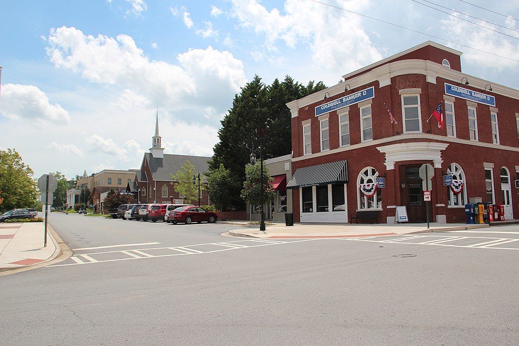 A brick corner building and street with a church under a cloudy sky. - Downtown Blue Ridge – Aska Road loop from Ellijay