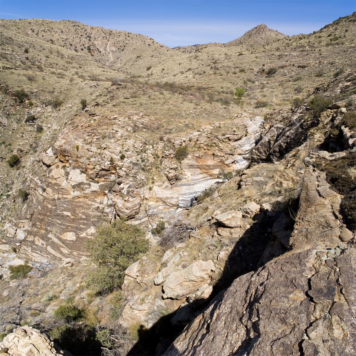 Arid mountain landscape with a deep, rocky canyon and sparse vegetation under clear sky.