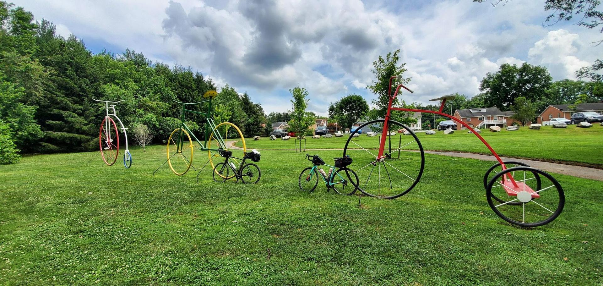 Artistic bicycle sculptures of various sizes on a green lawn, cloudy sky.
