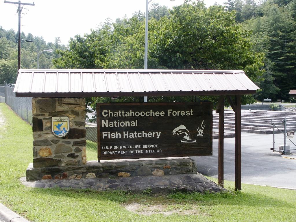 A large wooden sign with a stone base stands in a grassy area.