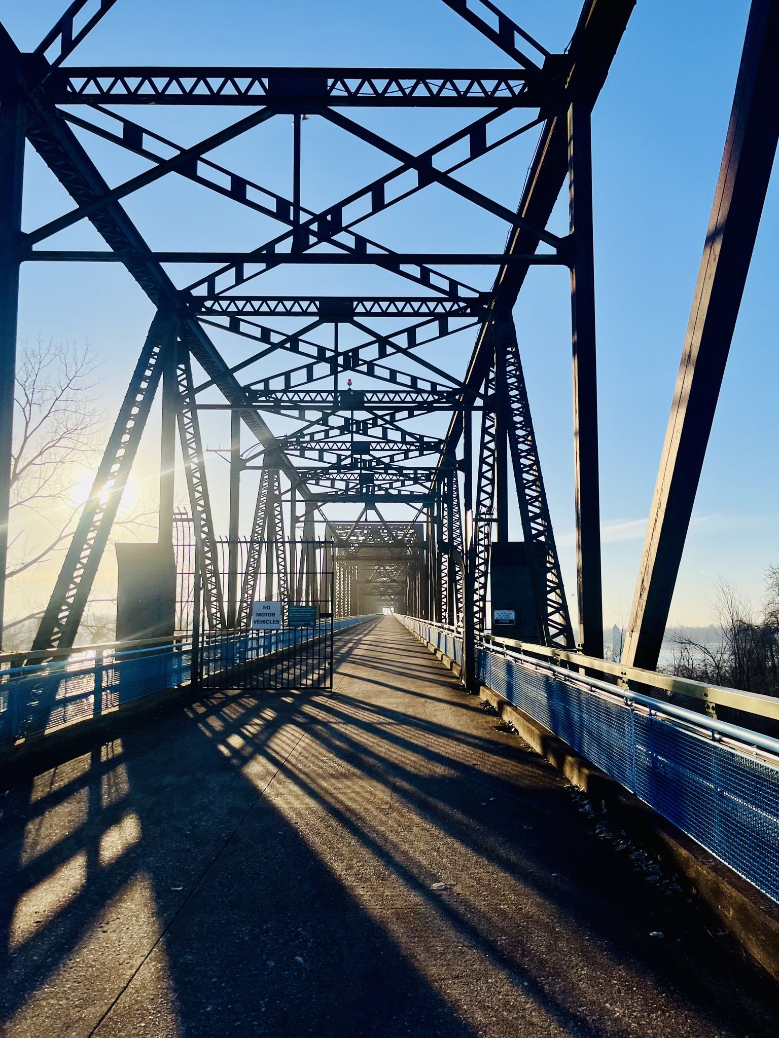 Sunlight streams through a metal truss bridge, casting long shadows. - Mississippi River Trail: St. Louis Loop