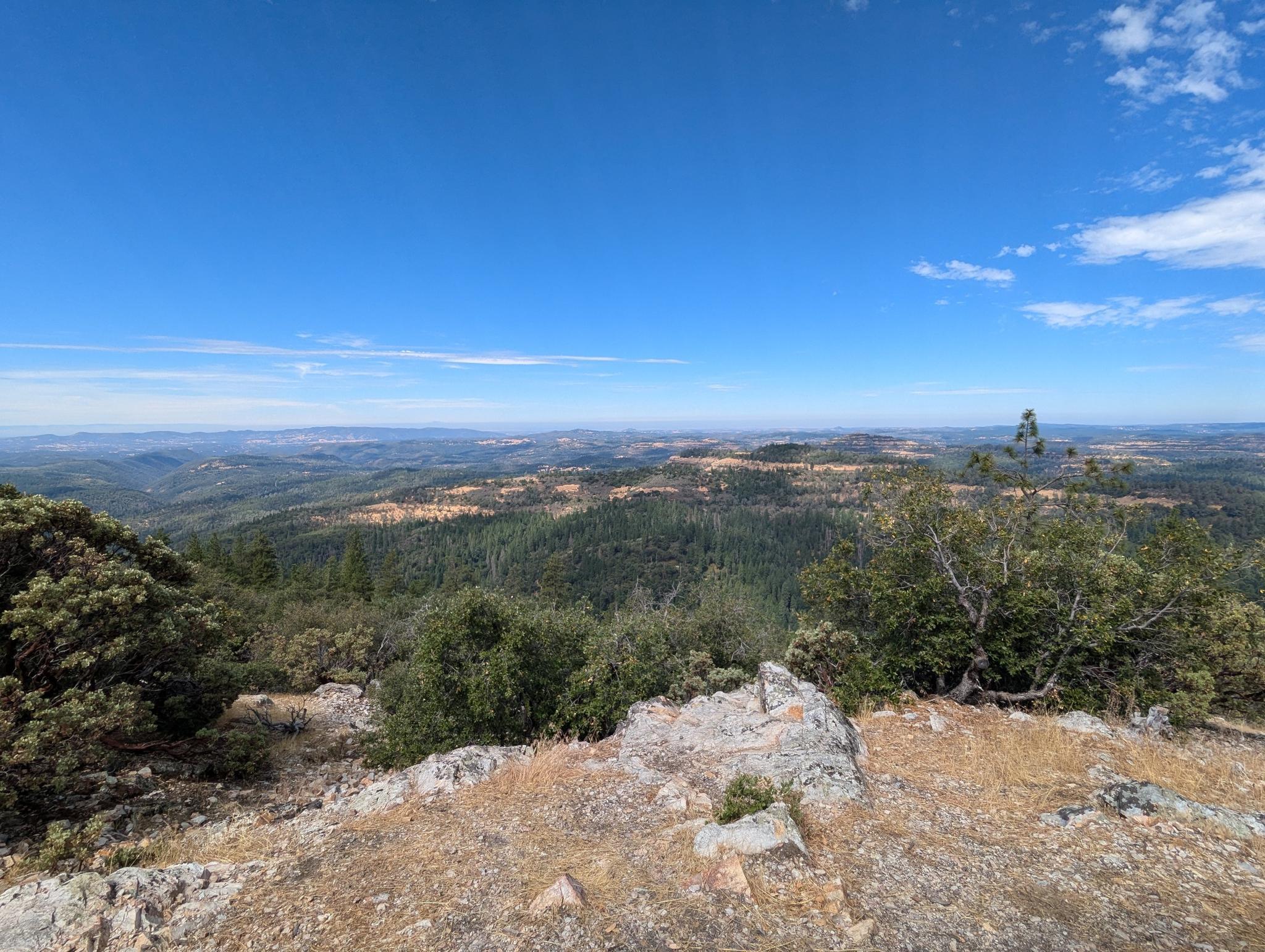 Expansive view from a rocky overlook of rolling forested hills under a clear blue sky.