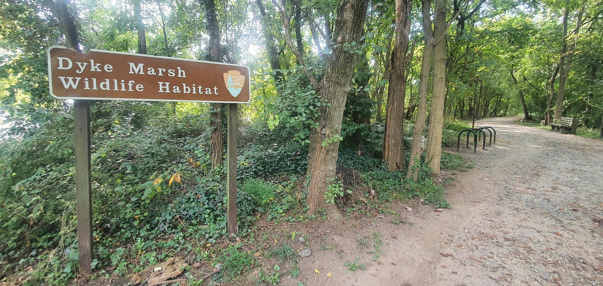 Brown sign for a wildlife habitat next to a dirt path in a forest.