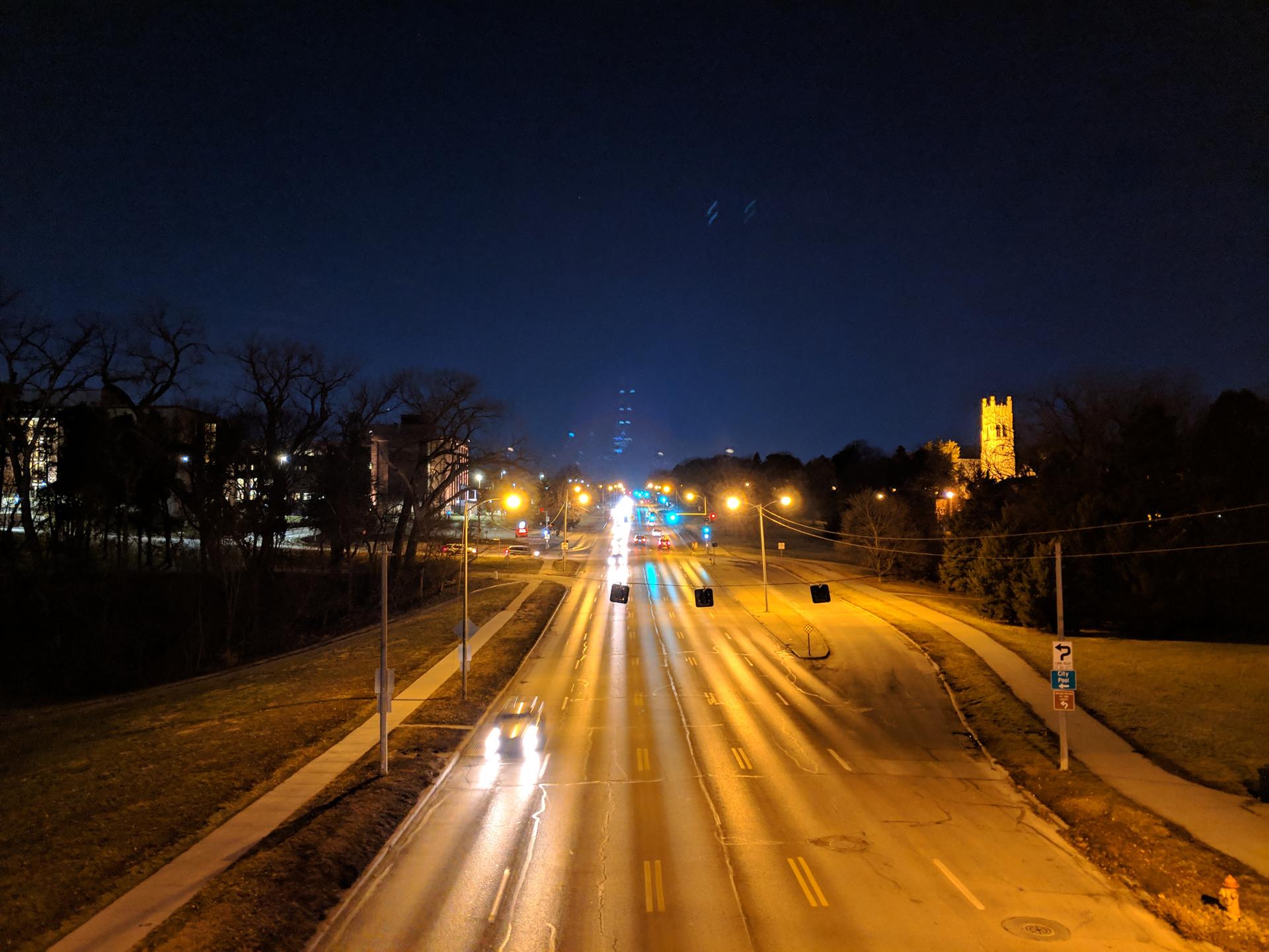 Nighttime view of a busy road with bright car lights and streetlights.