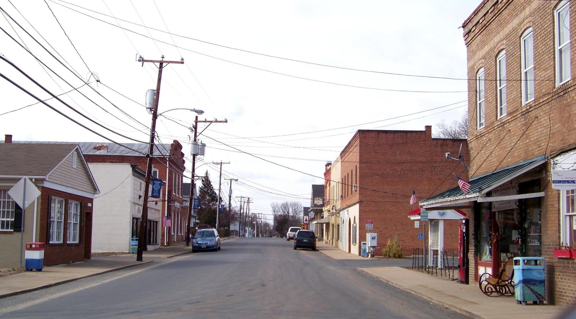 Empty small town street with brick buildings and utility poles under a bright sky.