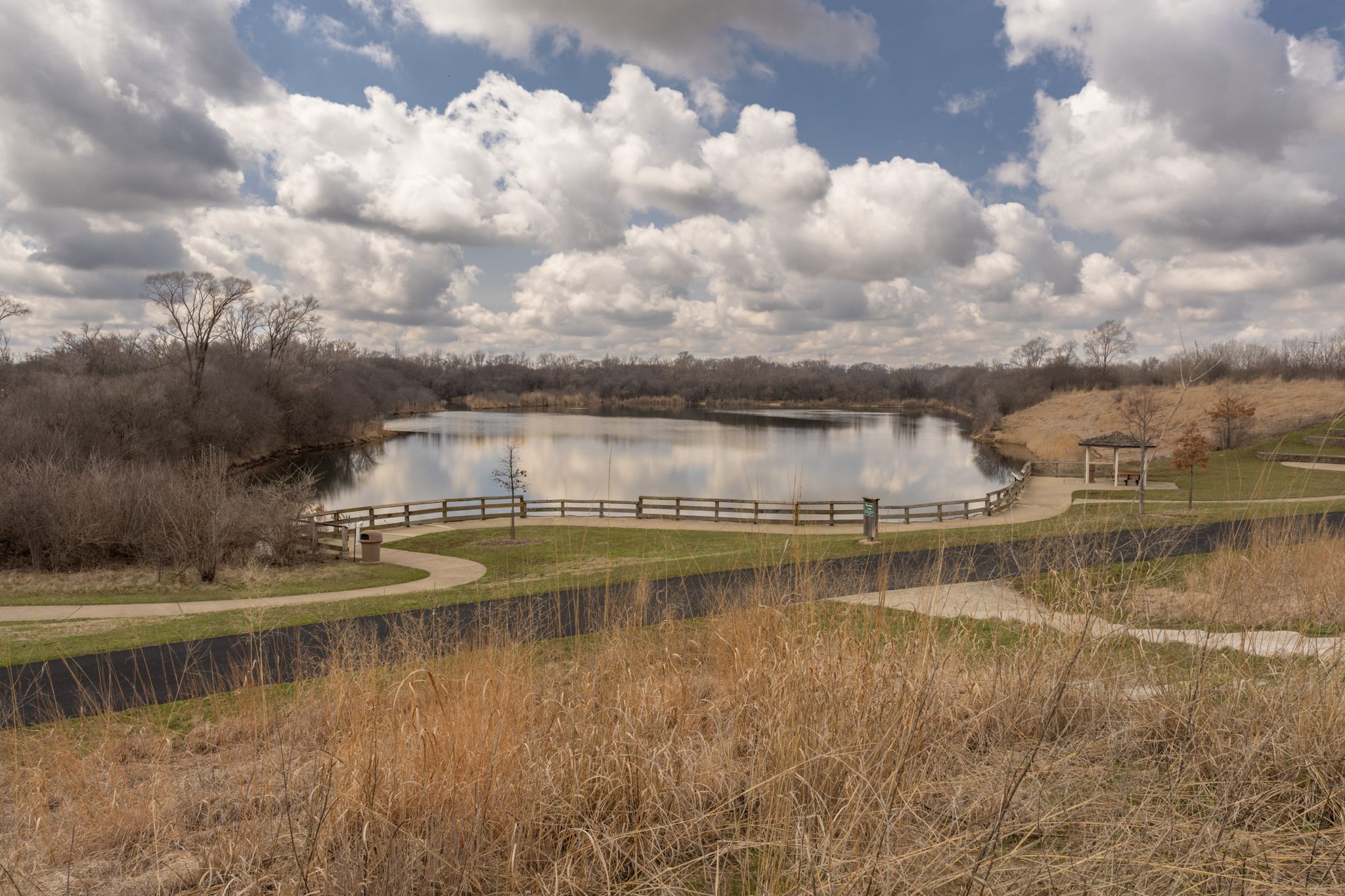 Overcast view of a lake with a path, gazebo, and bare trees. - Lake Renwick Bikeway
