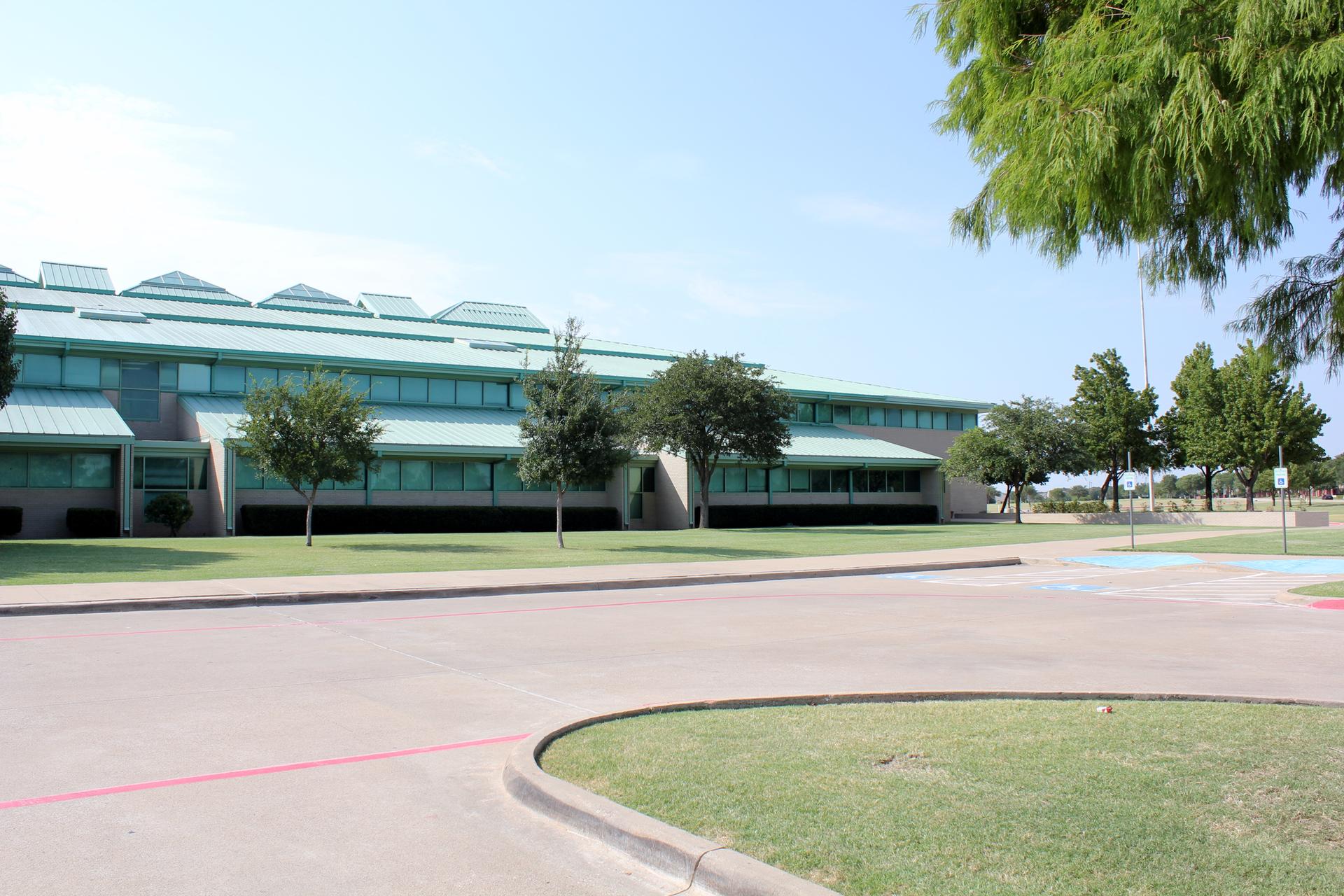 Modern building with green roof, paved lot, and scattered trees.