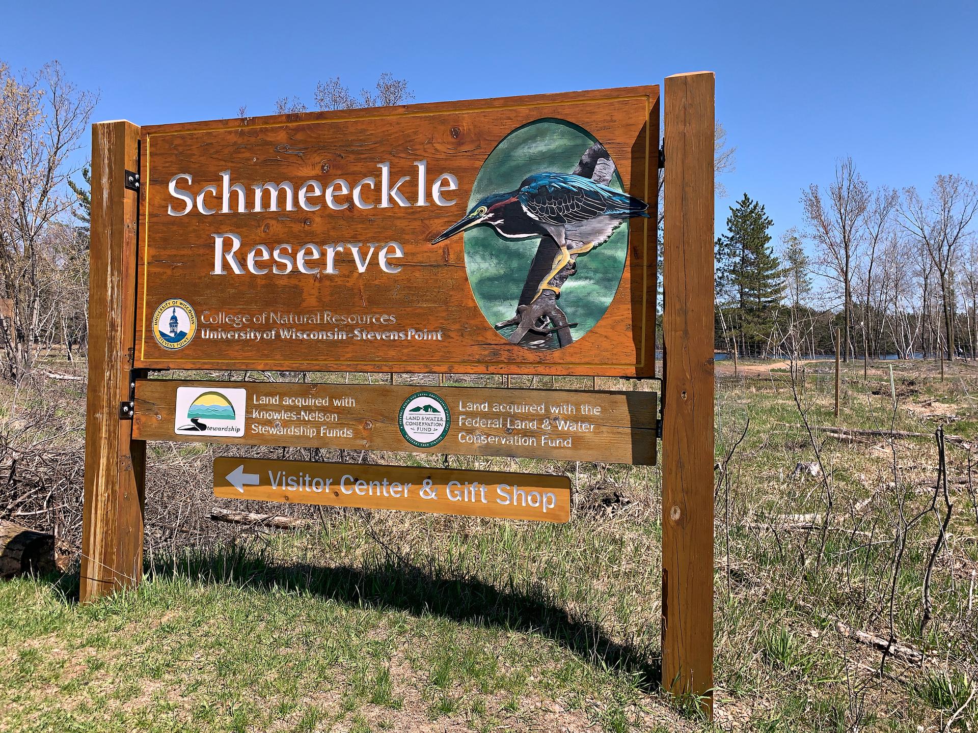 A wooden sign with a bird illustration stands on grassy ground under a clear sky.