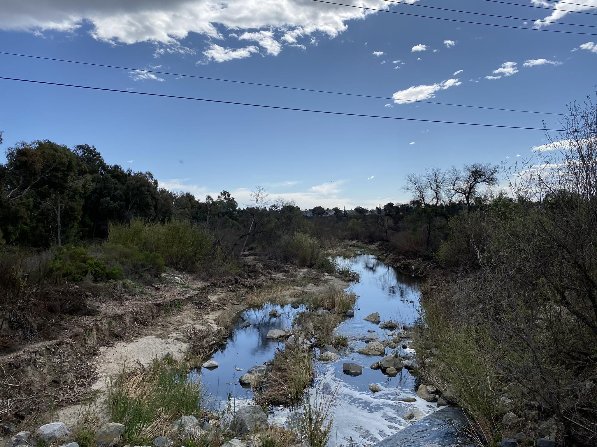 A river winds through a lush, rocky landscape under a bright, cloudy sky. - Aliso Creek and Pecten Loop Trail