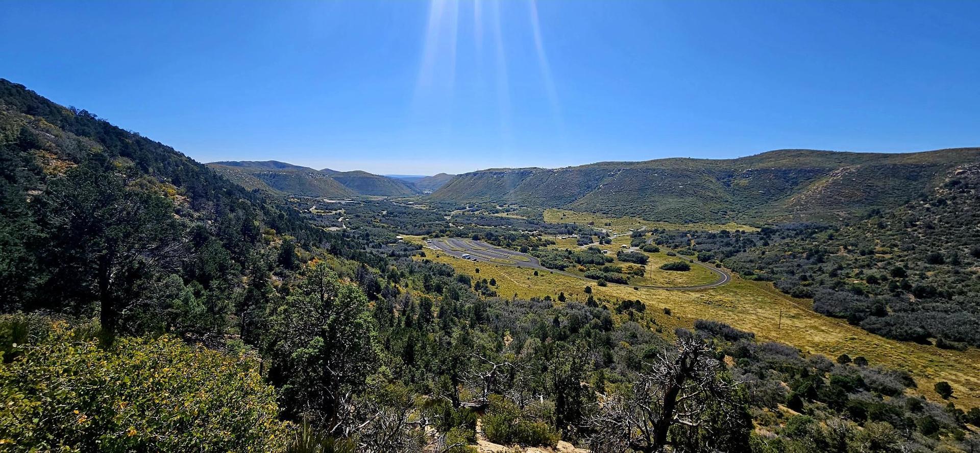 Sunny panoramic view of a green valley with distant buildings and mountains.