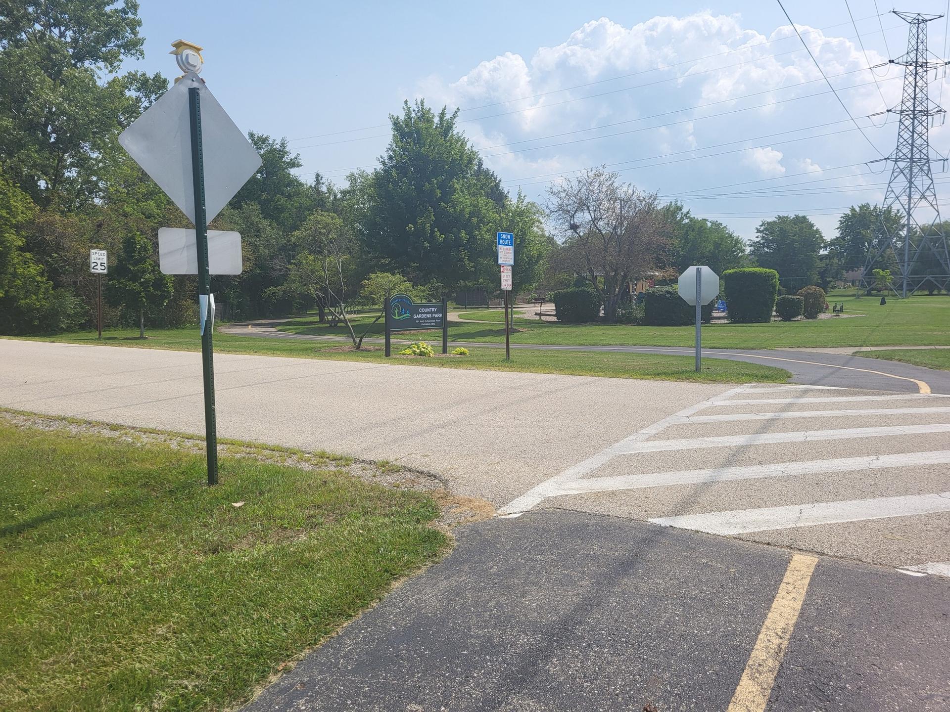 Intersection of paved paths and a crosswalk, with signs under a cloudy sky.