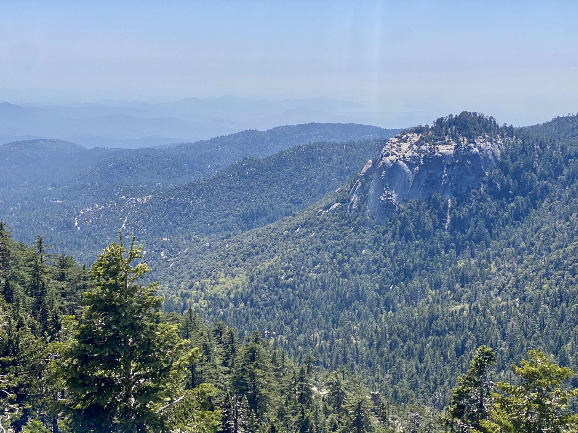 Hazy mountain range with dense green forests and a prominent rocky peak.