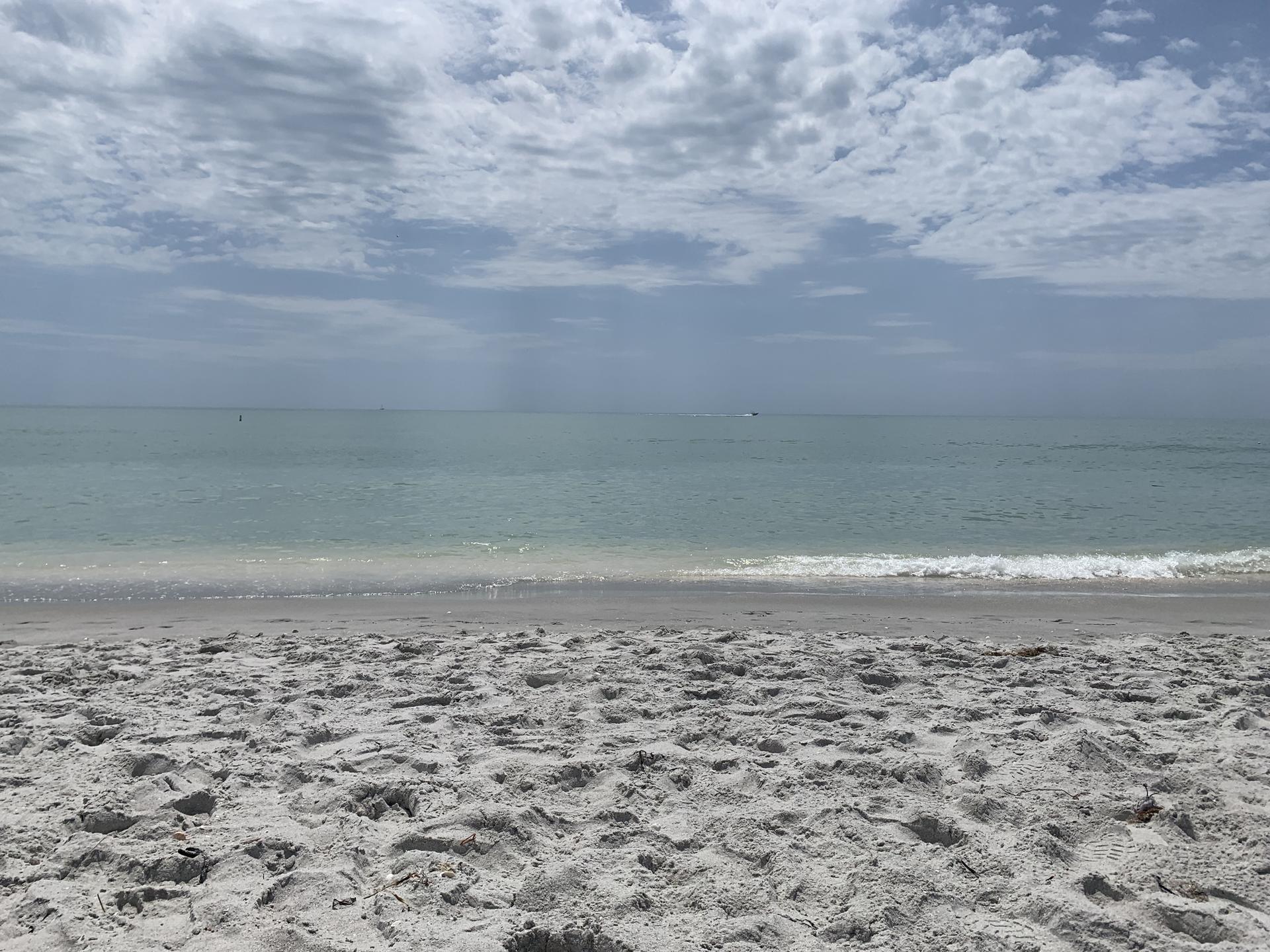Wide sandy beach meeting calm blue-green ocean under a cloudy sky.