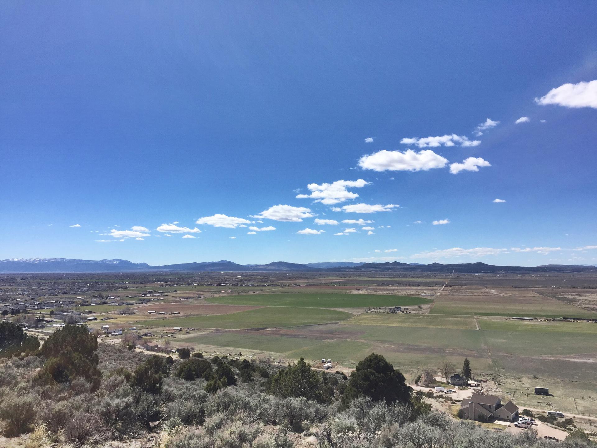 Panoramic view of a green valley and distant mountains under a bright blue sky.