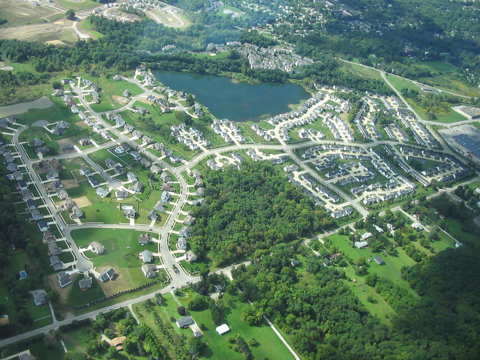 Aerial view of a suburban neighborhood surrounding a dark lake, green landscape.