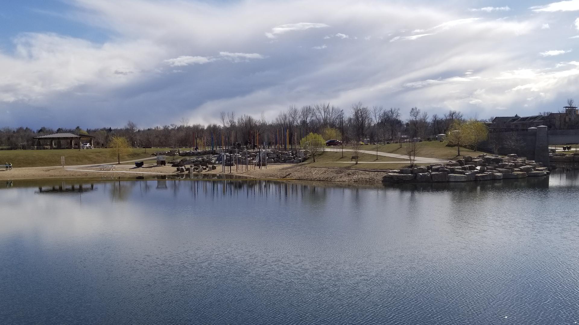Wide lake reflecting a cloudy sky, with a park and playground on shore.