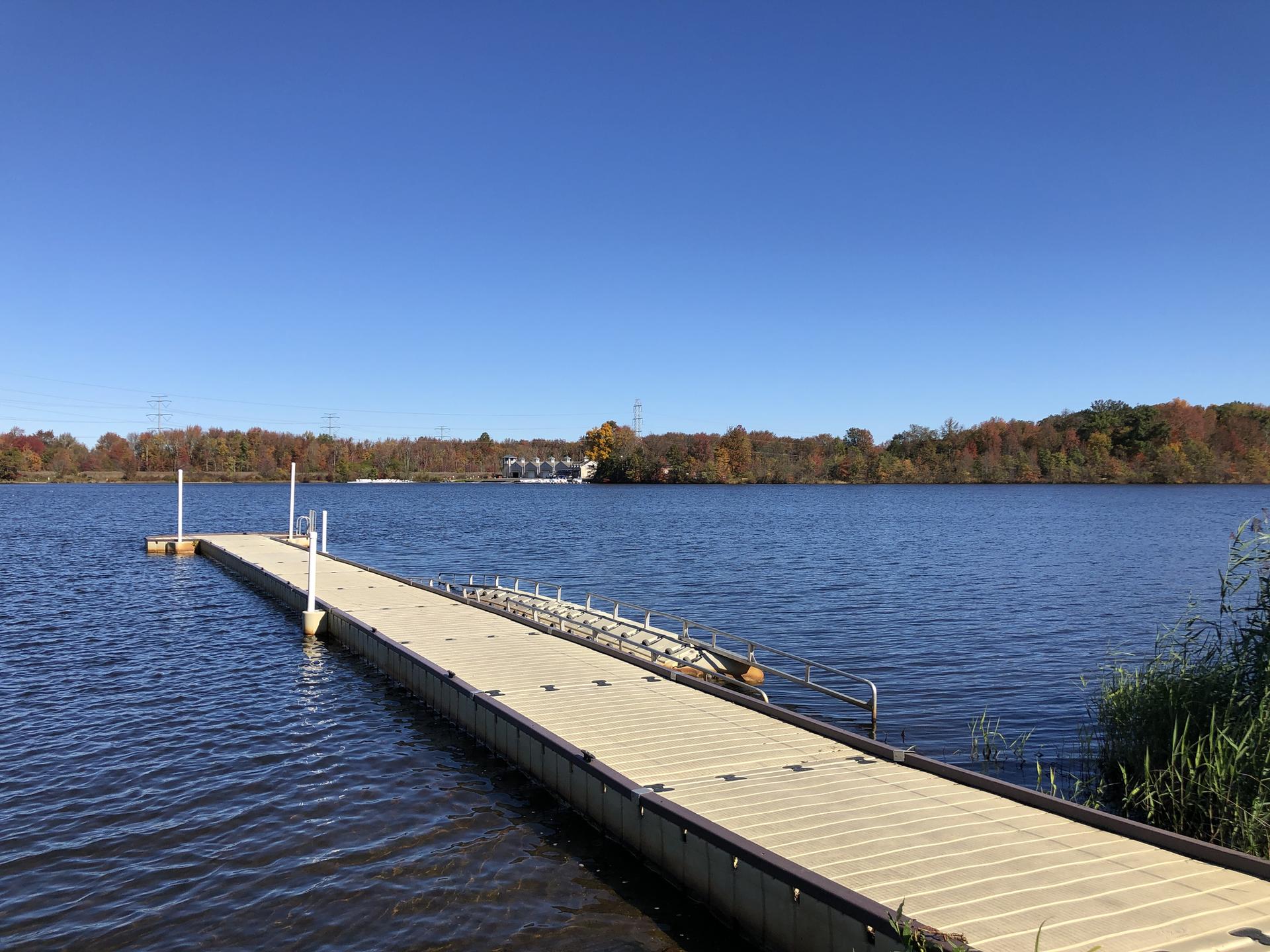A long dock extends into a calm lake under a bright blue sky.