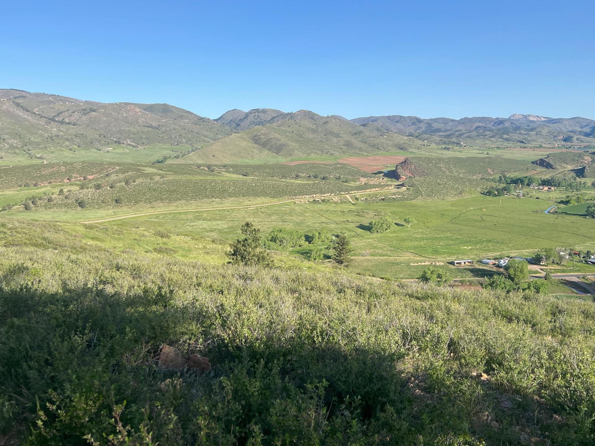 Expansive green valley with distant mountains under a clear blue sky. Sunny.