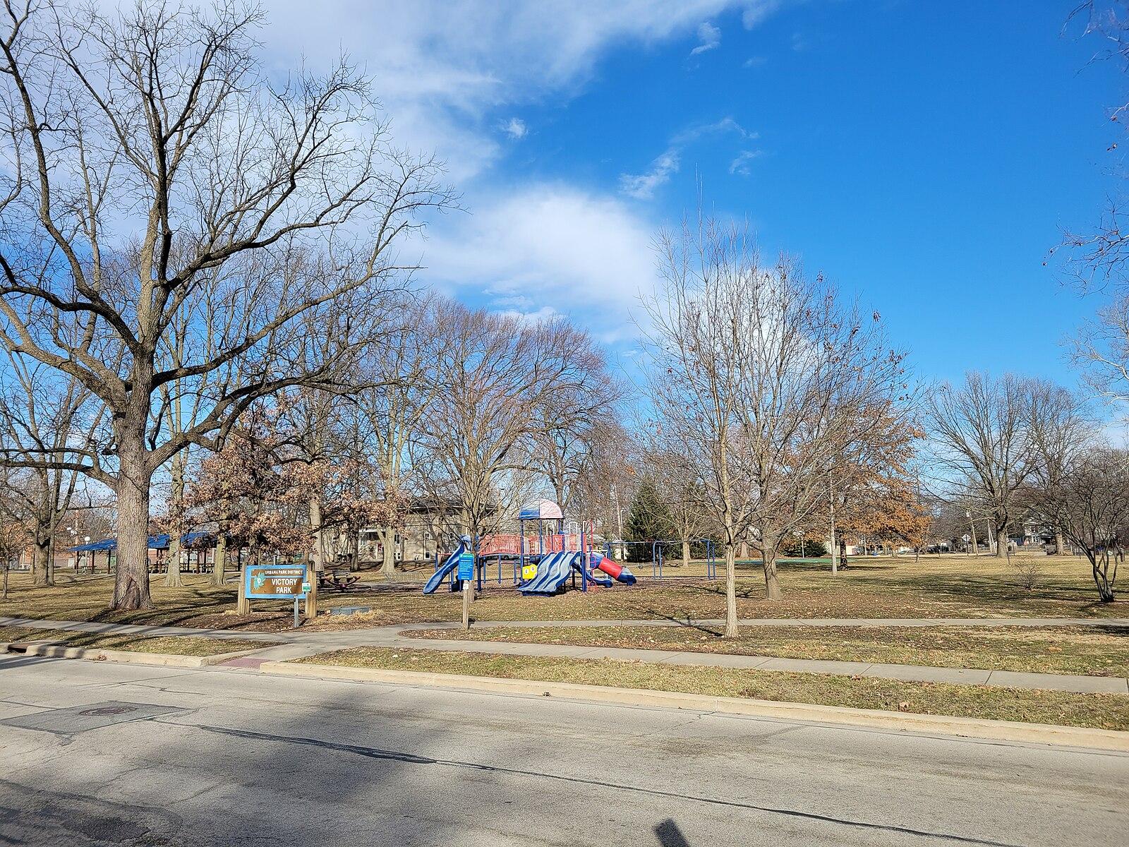 Bright sunny day over a park with a colorful playground and large trees.
