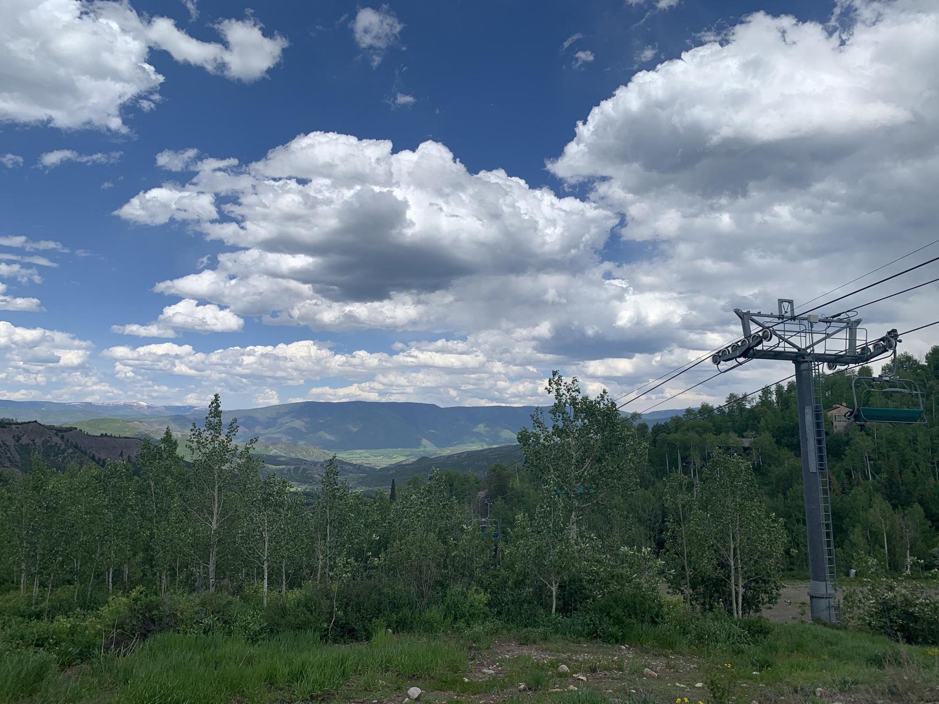 A ski lift tower overlooks a forested mountain landscape under a cloudy sky.