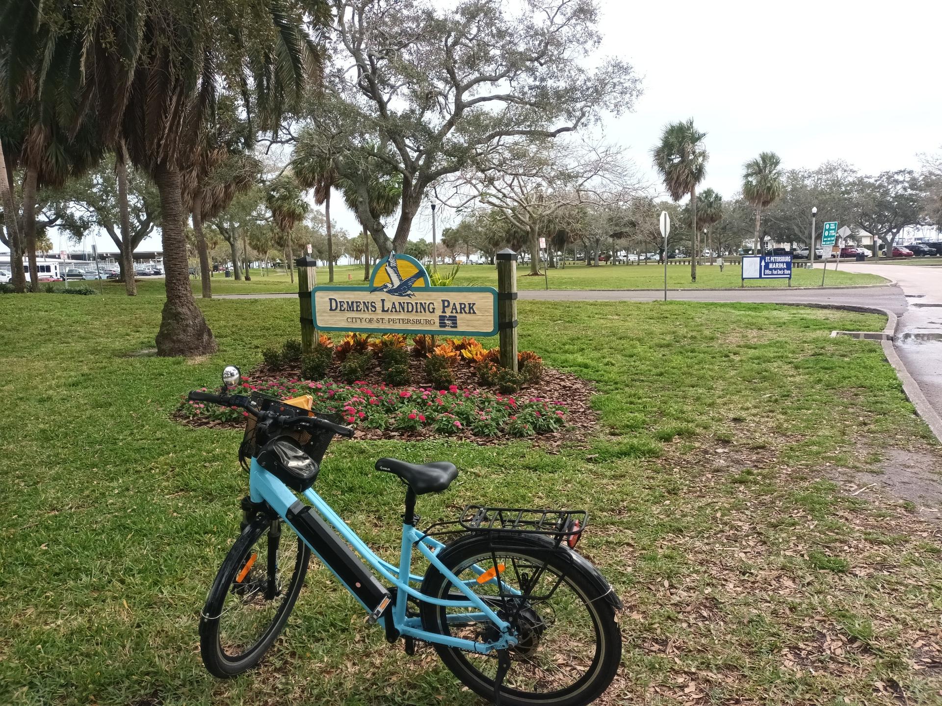 A blue bicycle parked near a park sign amidst green grass and trees.