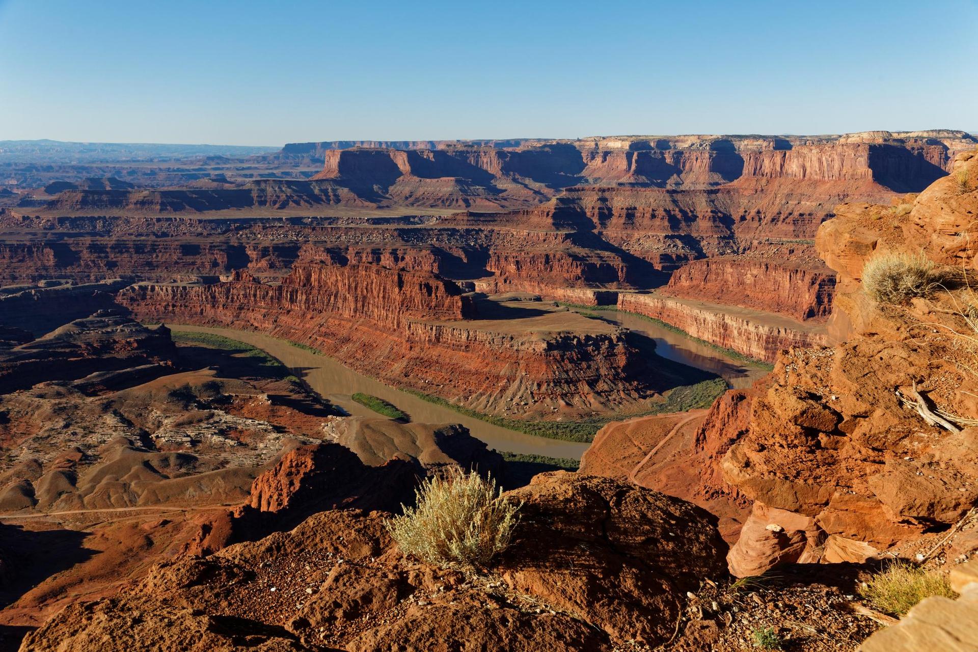 Expansive red rock canyon with a winding river under a clear sky.