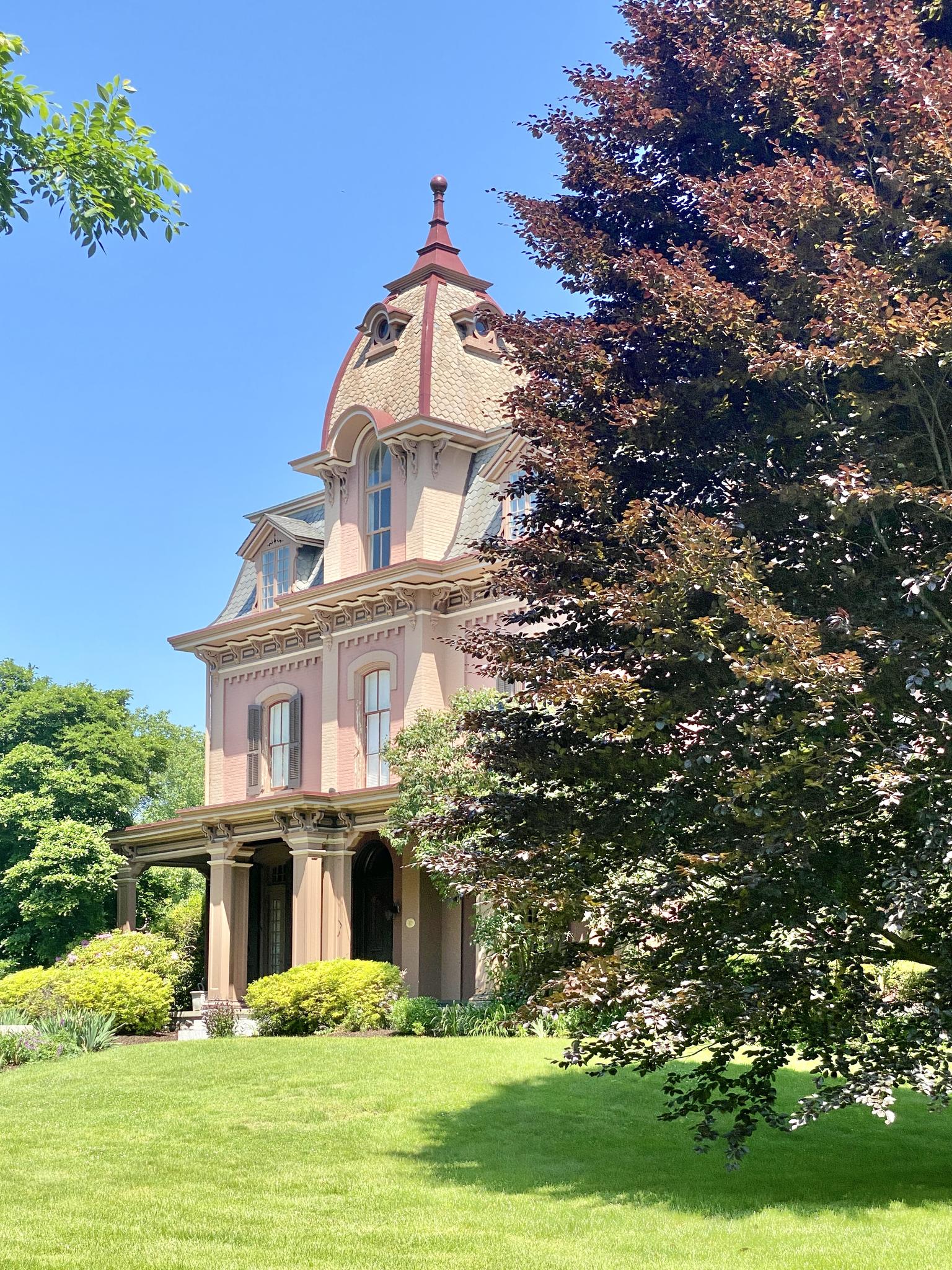 Ornate historic house with a unique roof, surrounded by green lawns and trees.