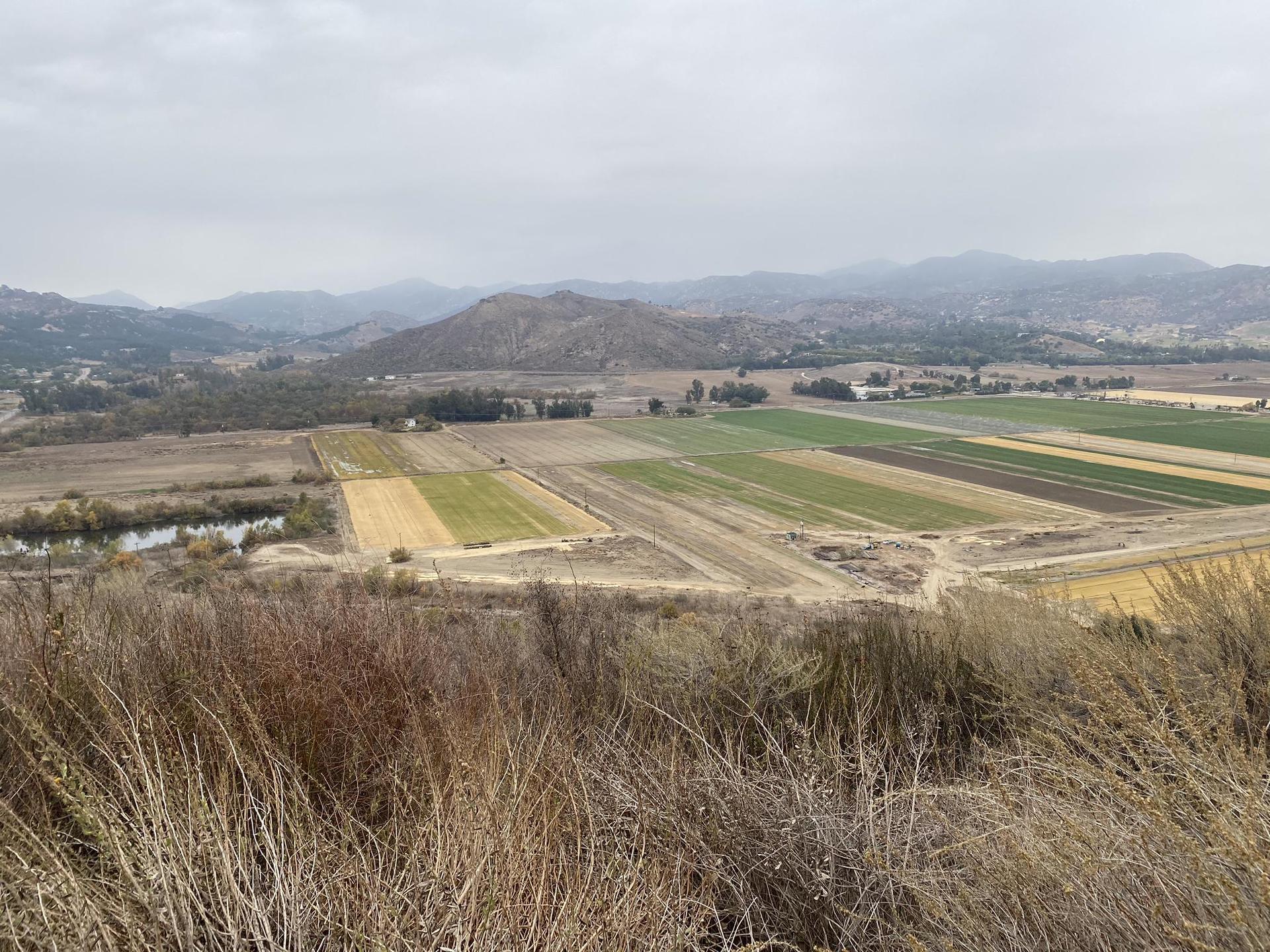 Overcast view of a valley with diverse agricultural fields and distant hills.