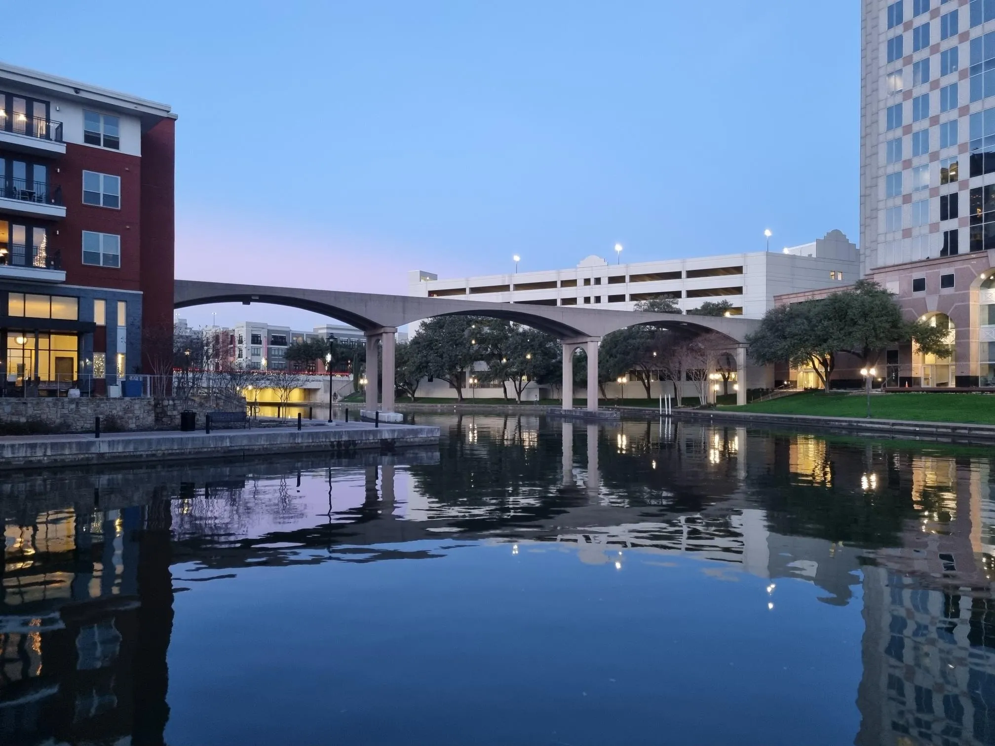 Evening view of a calm canal reflecting city buildings and an arched bridge. - Lake Carolyn Promenade