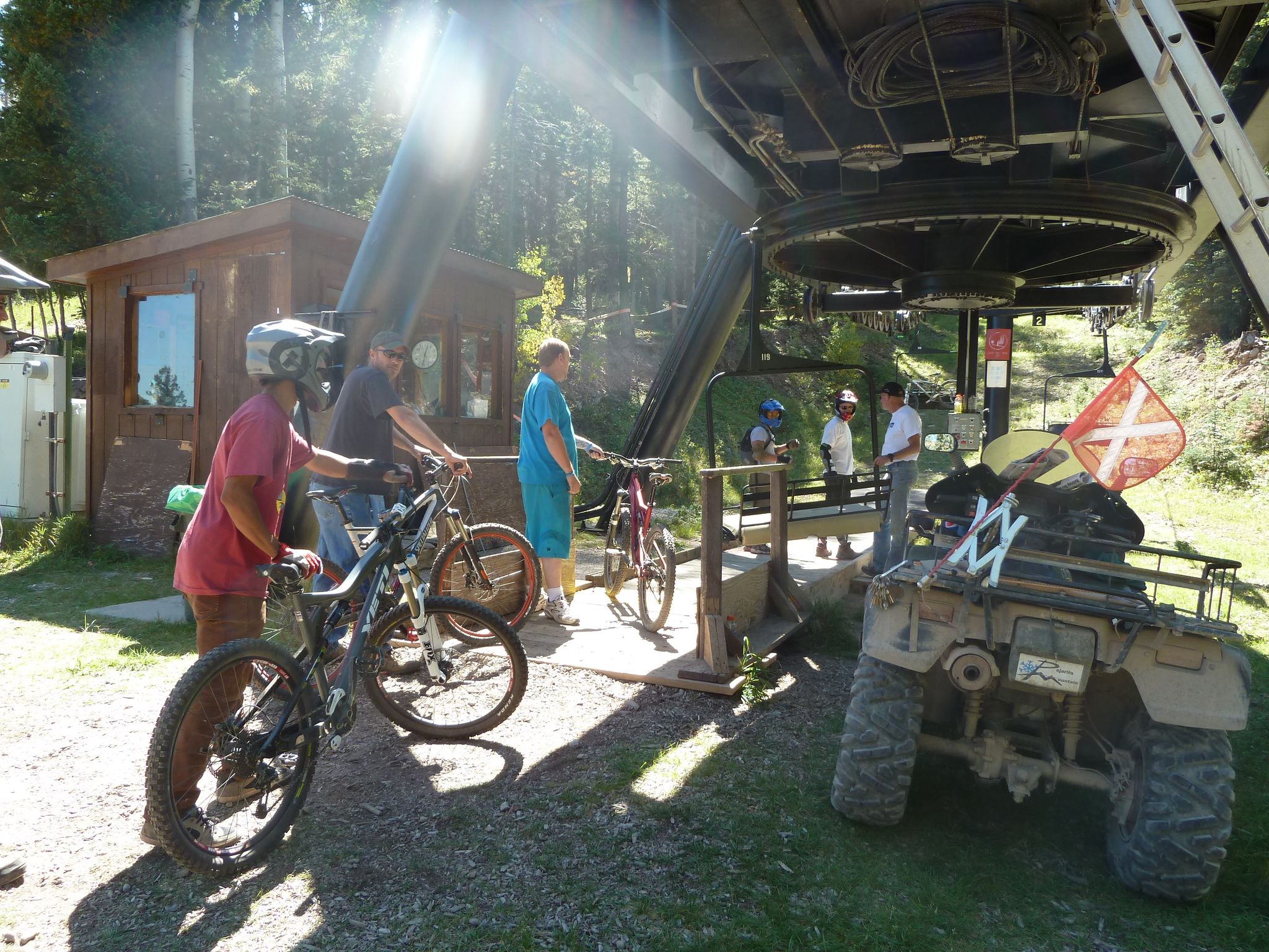 People with mountain bikes and an ATV near a ski lift base. - Pajarito Mountain loop