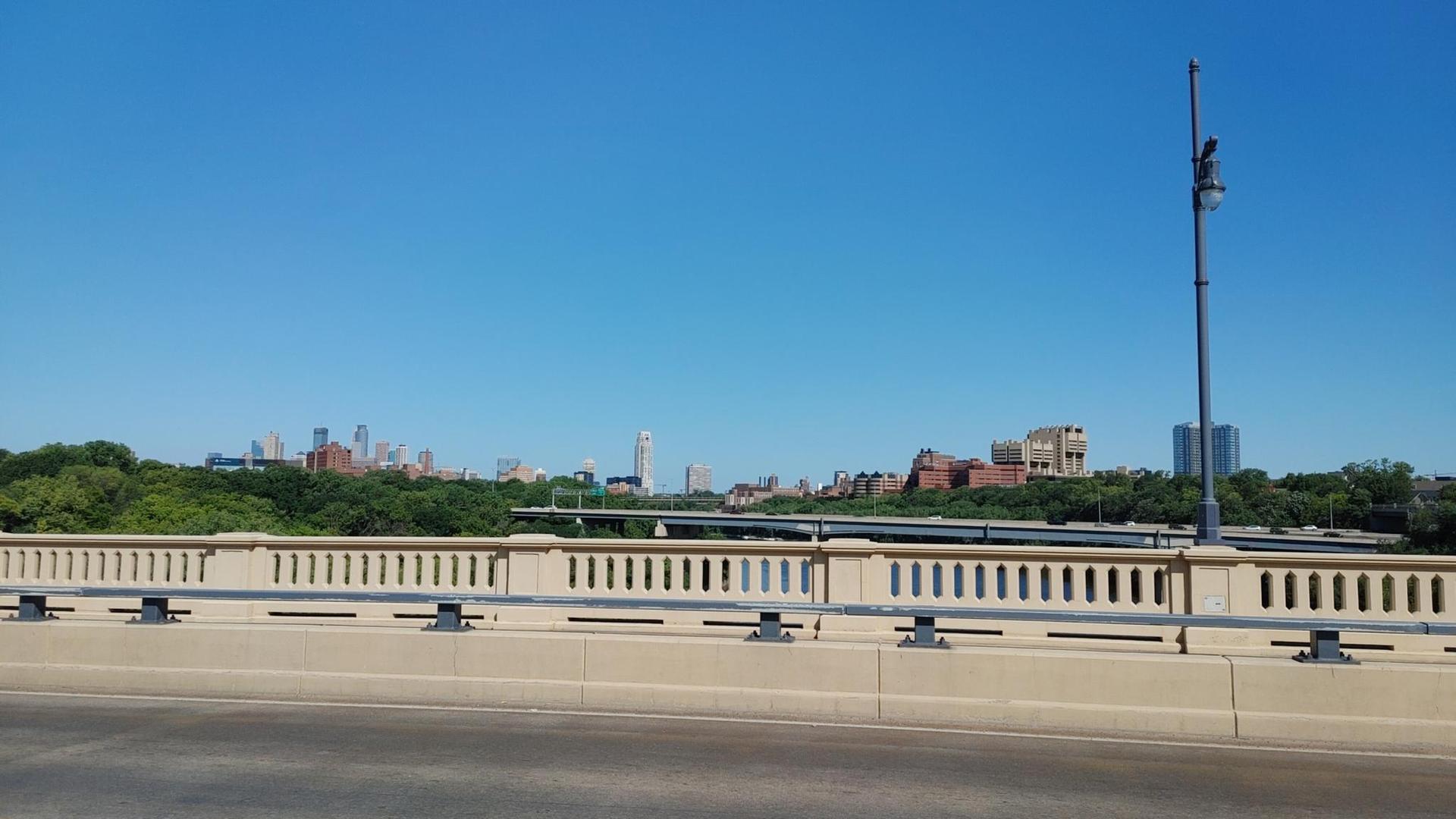 Bridge railing in foreground with a distant city skyline under a clear blue sky.