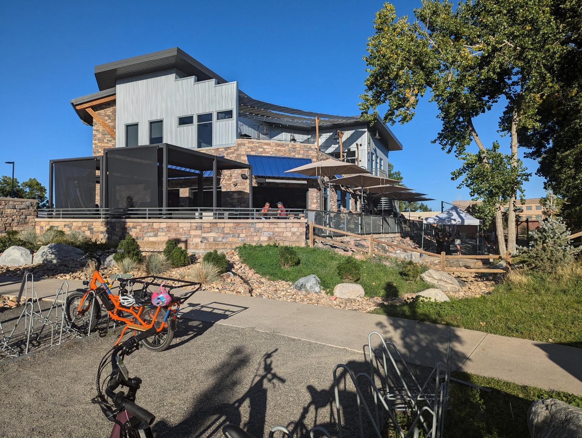 A modern building with an outdoor patio, bicycles, and green trees on a sunny day.